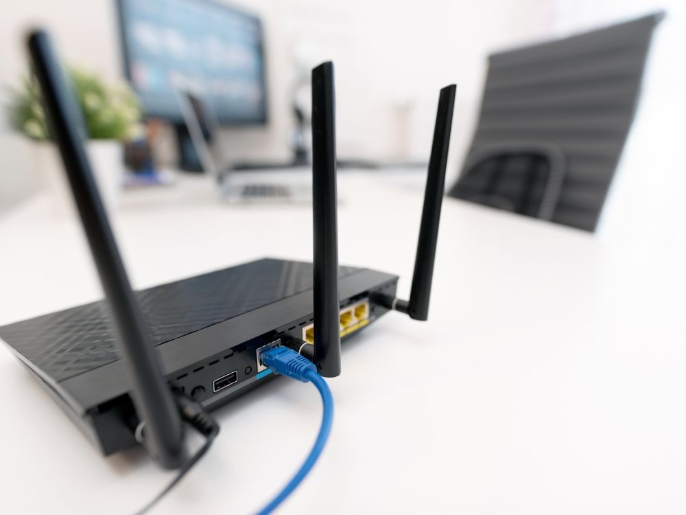 Roteador preto conectado por cabo de rede, simbolizando soluções práticas de como melhorar a internet do Wi-Fi.