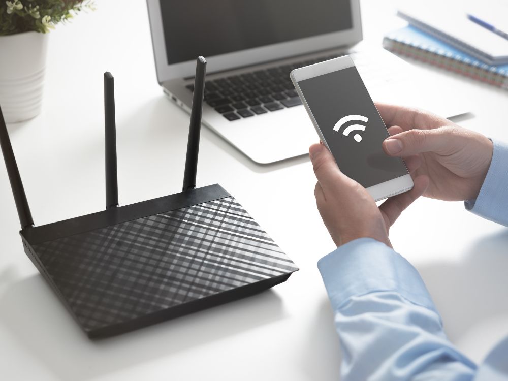Pessoa verifica sinal Wi-Fi em smartphone próximo a roteador, mostrando como o roteador influencia na velocidade da internet.
