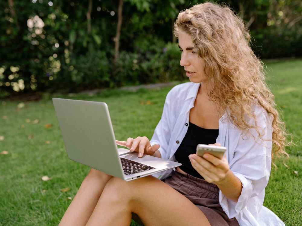 Mulher utilizando notebook ao ar livre mostrando dúvidas sobre Internet lenta como resolver quedas de sinal e baixa velocidade da conexão.