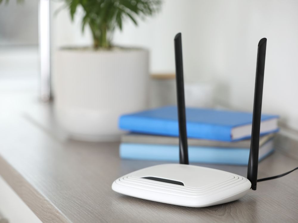 Roteador branco com antenas em cima de mesa, representando dicas de como melhorar a internet do Wi-Fi.