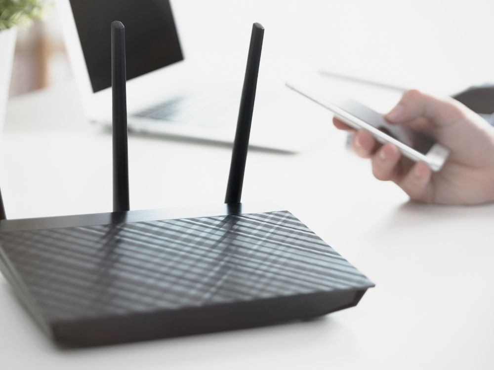 Roteador moderno com antenas e smartphone conectado ao Wi-Fi, exemplo prático de como a velocidade da internet depende do roteador e do uso simultâneo de dispositivos.