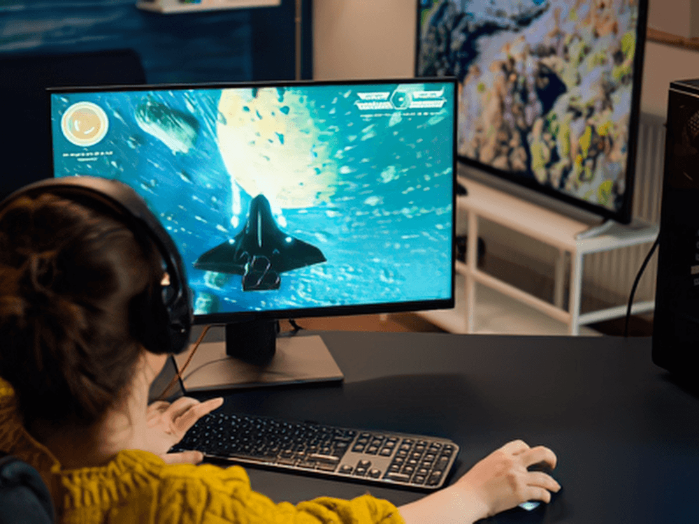 Pessoa joga em computador desktop com monitor gamer e headset, representando a necessidade de ter a melhor internet para jogos.