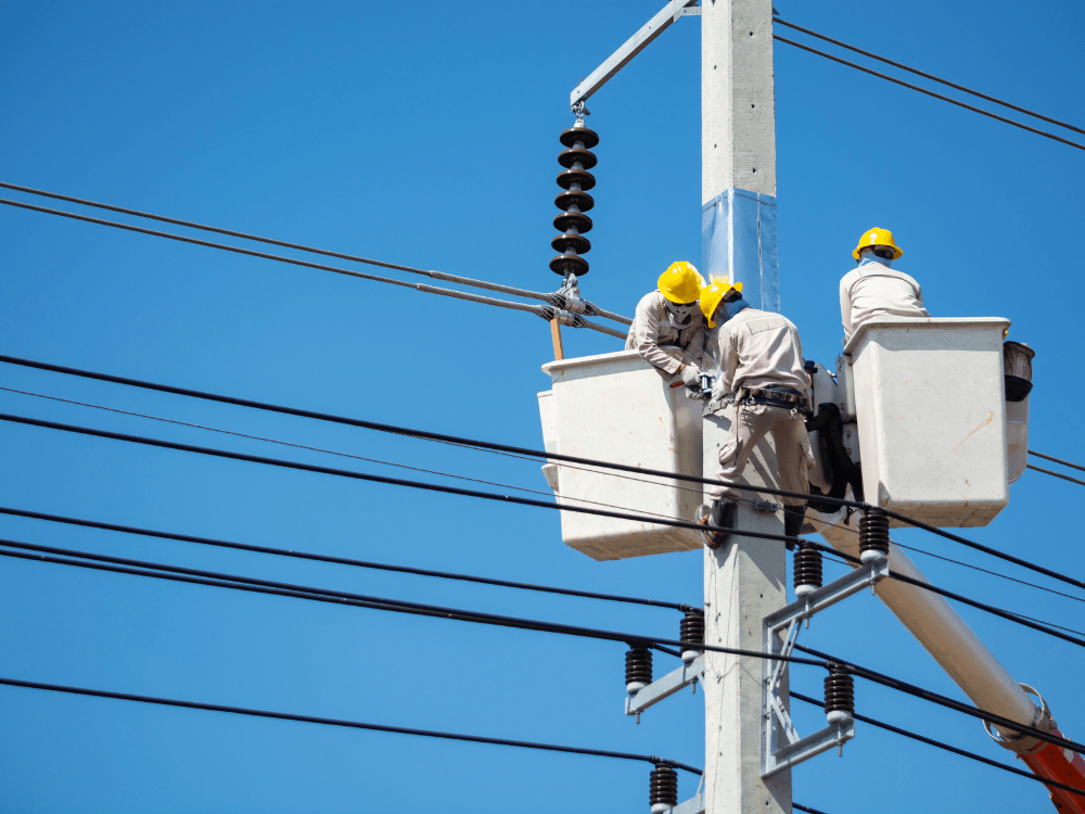 Equipe técnica realiza manutenção em poste com cabos aéreos, demonstrando a infraestrutura de fibra óptica junto com energia