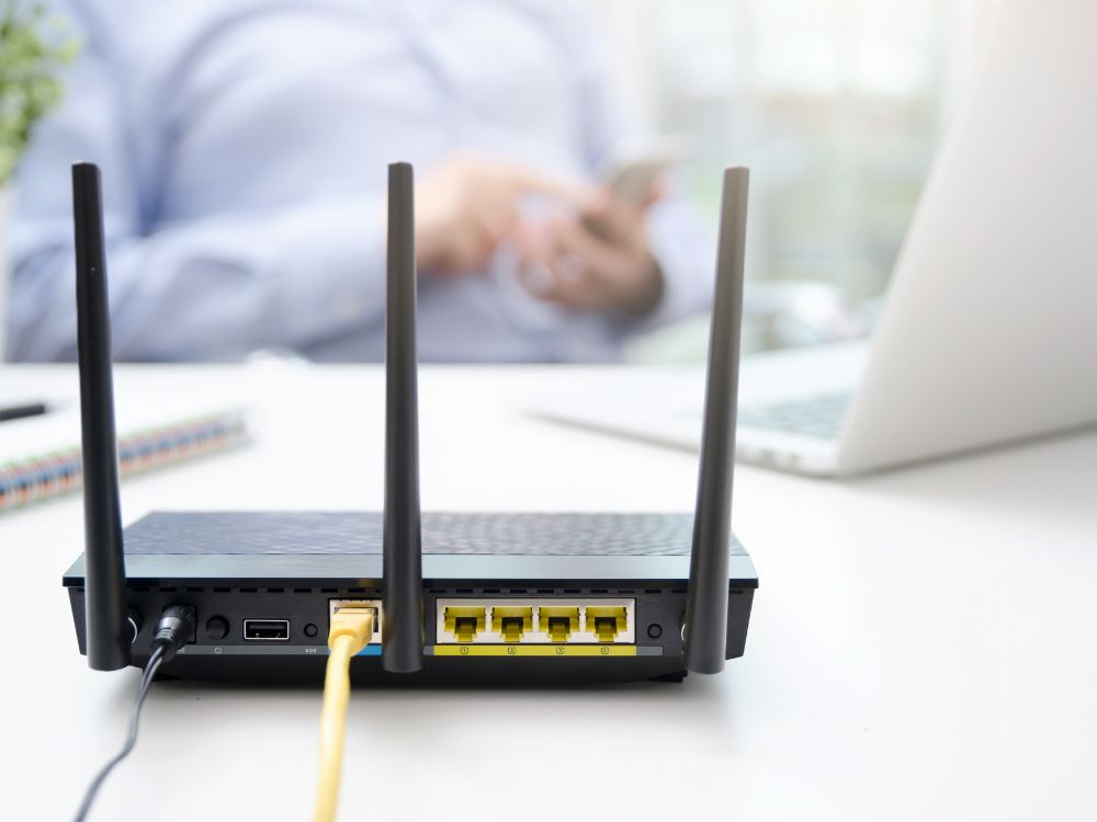 Roteador preto com cabos conectados sobre mesa de escritório. Equipamento de rede em destaque para explicar aspectos técnicos em Descubra o que causa interferência no Wi-Fi.