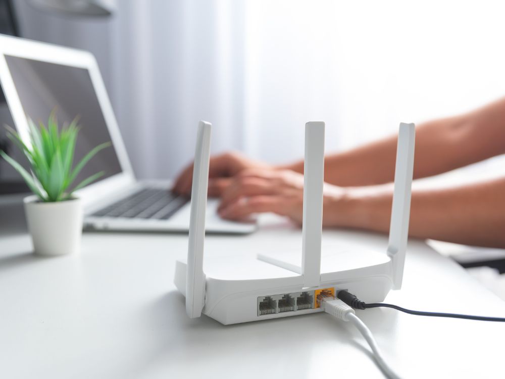Roteador Wi-Fi conectado ao notebook em ambiente de trabalho, mostrando como a velocidade da internet depende do roteador e da qualidade da conexão usada.