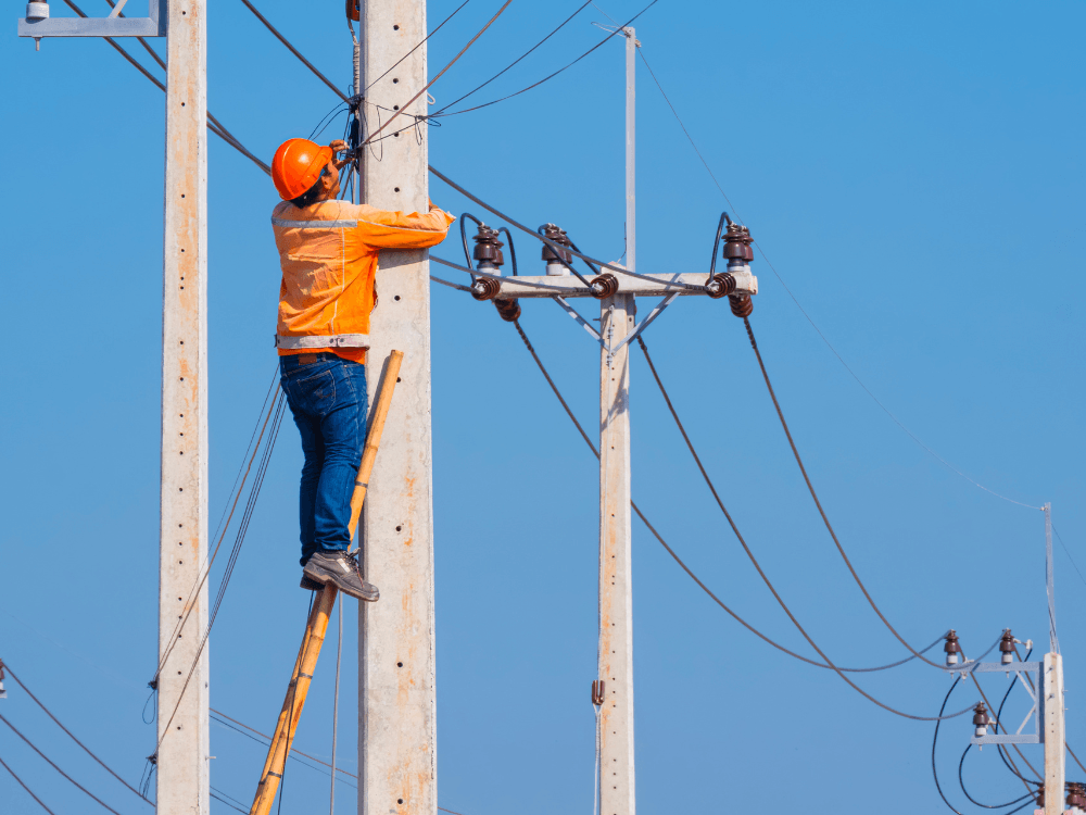 Técnico trabalha em um poste de energia realizando instalação de cabos, ilustrando o compartilhamento entre rede elétrica e fibra óptica.