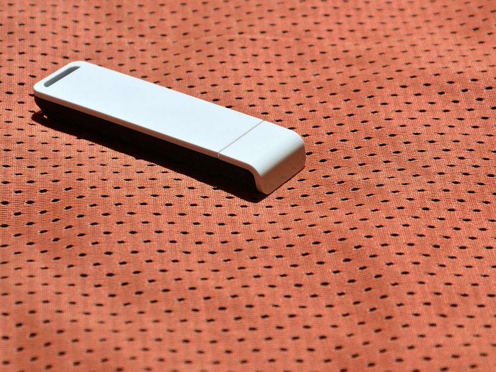 WiFi compacto, estilo pendrive, sobre superfície texturizada laranja. Entenda como funciona um adaptador WiFi prático e portátil.