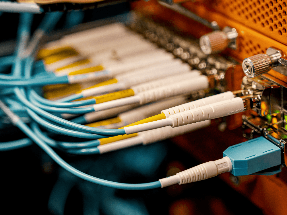 Cabos de fibra óptica conectados a equipamentos de rede demonstram a infraestrutura utilizada para fornecer internet de alta velocidade.