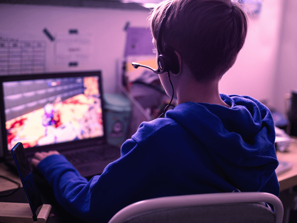 Pessoa utiliza headset enquanto joga em um notebook, destacando a importância de uma internet estável para partidas online.