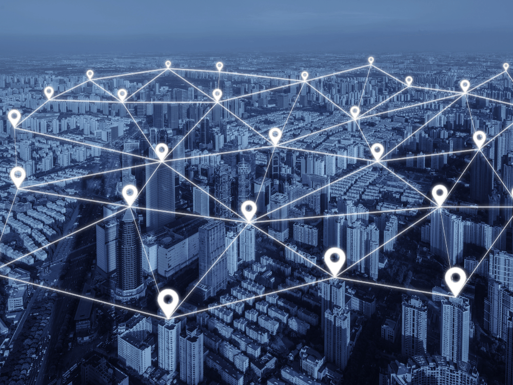 Vista aérea de uma cidade com pontos conectados por linhas digitais, ilustrando a infraestrutura de redes em ambientes urbanos.