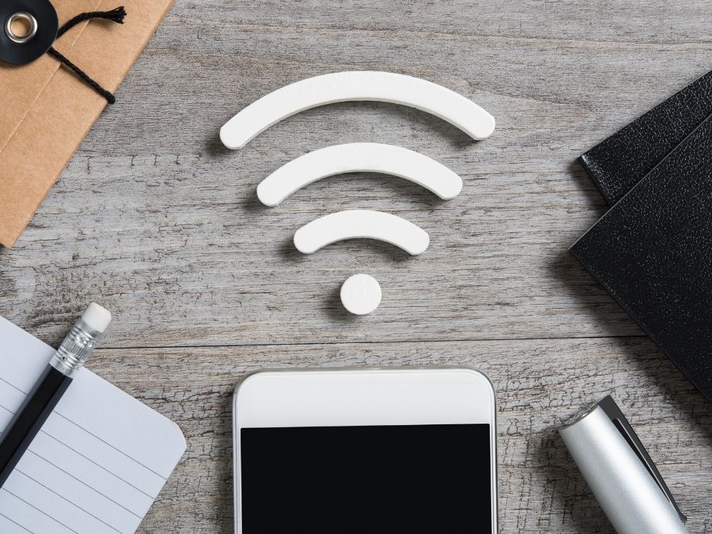 Símbolo de Wi-Fi sobre mesa ao lado de smartphone, lápis e materiais de escritório.